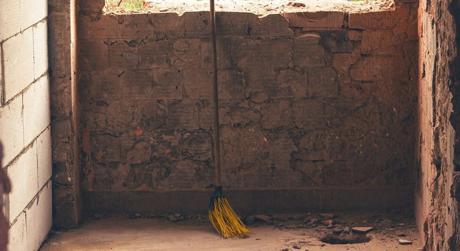 Post-construction cleaning, broom leaning against an unfinished brick wall, ready for after-build dust and debris cleanup